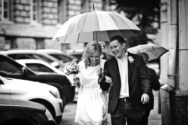 Gli sposi che ridono camminano sotto un ombrello per la città — Foto Stock