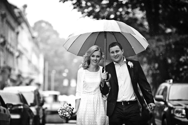 Schöne Frischvermählte lächeln beim Gehen unter einem Regenschirm — Stockfoto