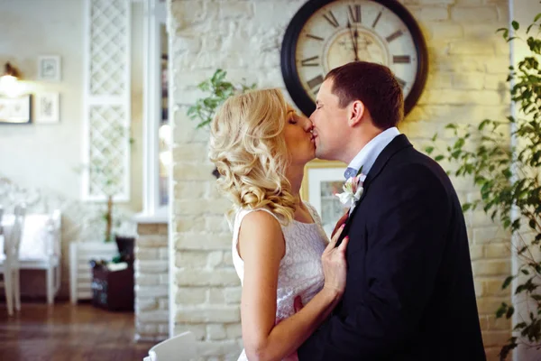Sposo baci bionda sposa tenera mentre in piedi sotto un orologio — Foto Stock