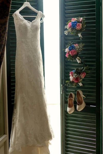 Peg with wedding dress, shoes and bouquets hang over the green d