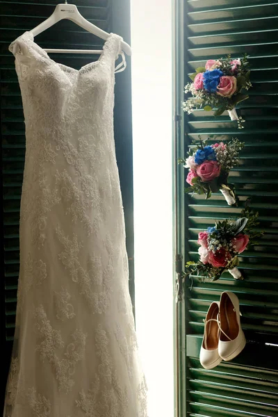 Hermoso vestido de novia cuelga en las puertas verdes detrás de los zapatos y bo —  Fotos de Stock