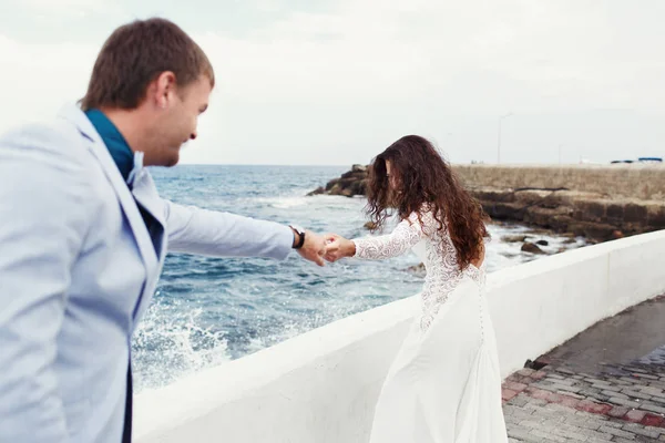Brunette noiva com cabelos longos segura a mão do noivo firmemente enquanto w — Fotografia de Stock
