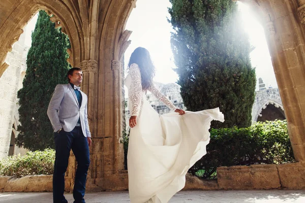 Bride whirls in the front of a groom under the stone archs — Stock Photo, Image