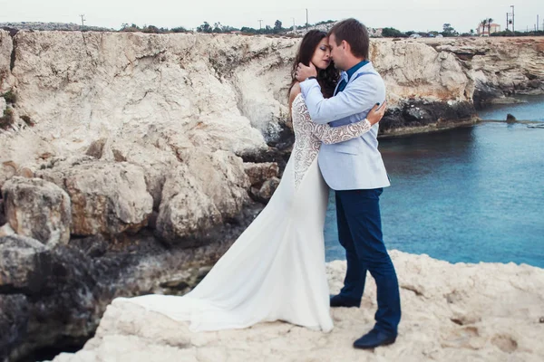 Largo vestido blanco yace en la roca mientras la mujer abraza a un hombre —  Fotos de Stock