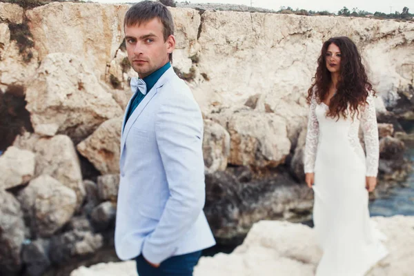 Stijlvolle bruidspaar staat tussen de rotsen door de zee — Stockfoto