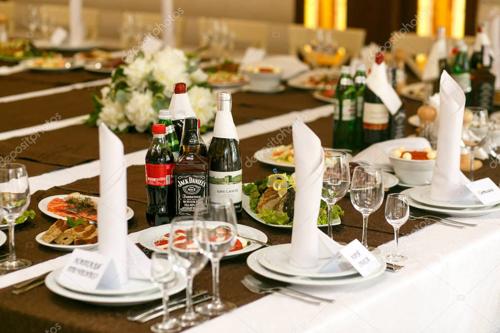 Drinks stand between white plates on brown  tablecloth