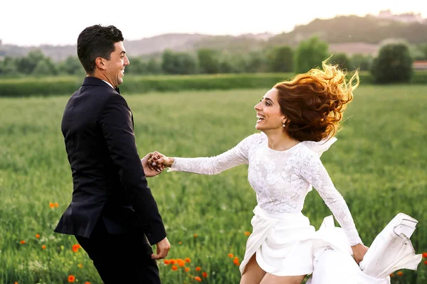 Lockigt brud ser på en groom medan de hoppar på fältet — Stockfoto