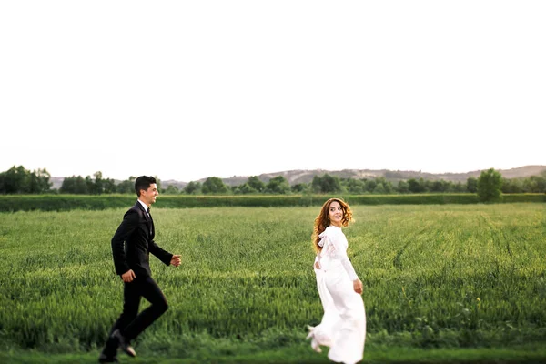 Groom essaie d'attraper une mariée courant autour du champ vert — Photo