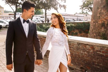 Tuğla duvar boyunca bir damat ile gelini baştan çıkarıcı elbise yürür