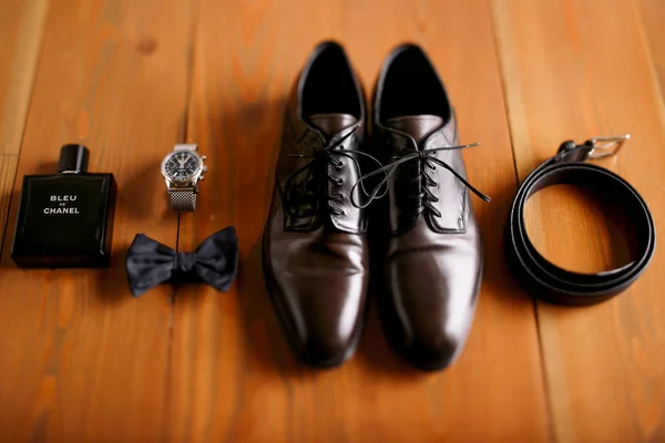 Classy leather shoes, belt, bow tie and watch lie on the wooden