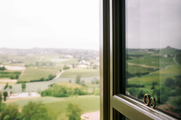 Trauringe stehen am Fenster, hinter dem sich wunderschöne — Stockfoto