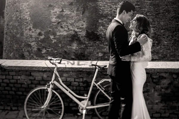 Dreamy wedding couple stands at the bicycle behind the wall — Stock Photo, Image