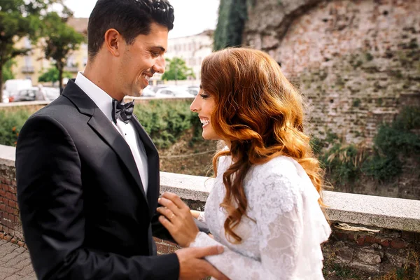 Riendo novia con el pelo rojo se pone delante de un novio en la calle — Foto de Stock