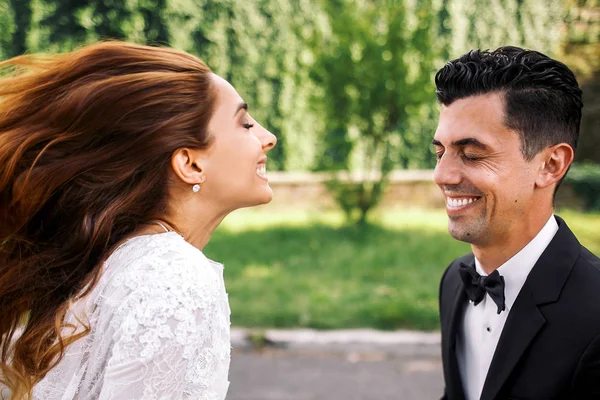 Вітер дує волосся нареченої, поки вона посміхається до нареченого — стокове фото