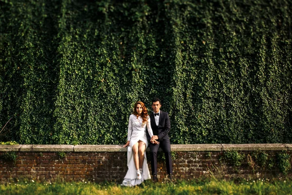 Bruid en bruidegom met naakte benen zitten op de bakstenen muur — Stockfoto