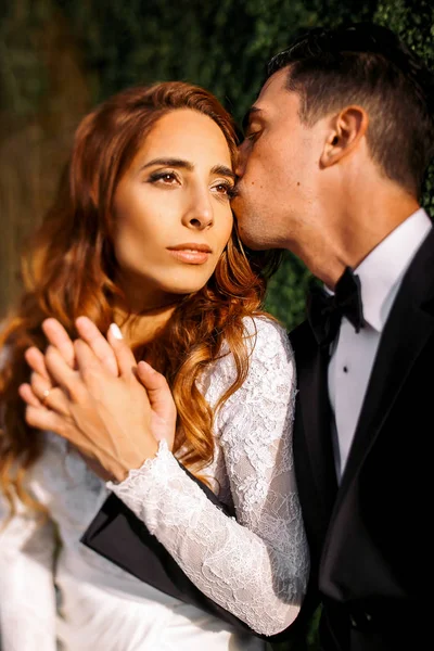 Evening sun illuminates gorgeous bride's face while groom kisses — Stock Photo, Image