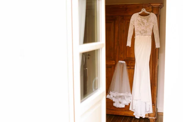 Vestido blanco y velo corto cuelgan de la puerta de madera —  Fotos de Stock