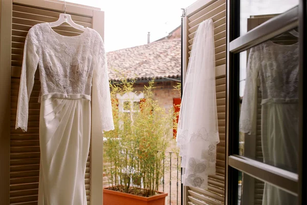 Elegante vestido de novia y velo cuelgan en las puertas del balcón —  Fotos de Stock