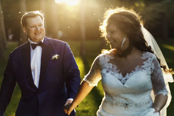 Glücklicher praller Bräutigam blickt eine Braut an, während sie über den Rasen läuft — Stockfoto