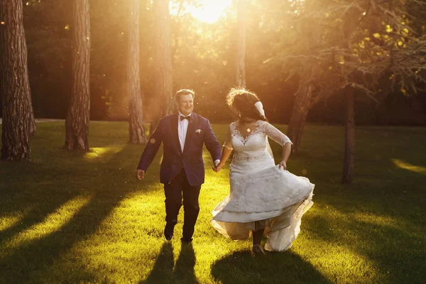 Braut wird zu lustigem Bräutigam, der mit ihr über den Rasen rennt — Stockfoto