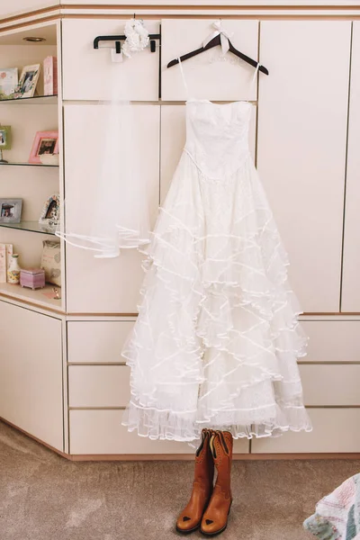 Botas de vaquero de pie bajo hermoso vestido de novia —  Fotos de Stock