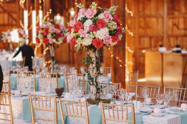 Ahşap hangarda yemek masalarında pembe buketleri standı