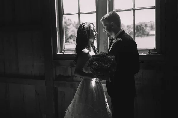 Groom holds wedding bouquet while looking at a bride in the ligh — Stock Photo, Image