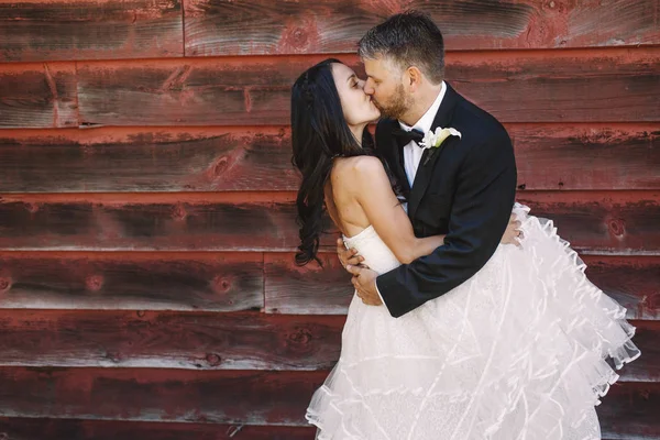 Braut hüllt Bräutigam in ihr lockiges Kleid ein, während er sie küsst — Stockfoto