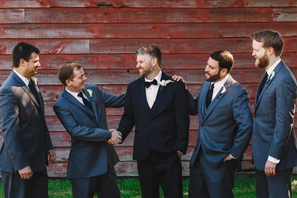 Os padrinhos de ternos azuis cumprimentam o noivo enquanto posam diante de uma madeira — Fotografia de Stock