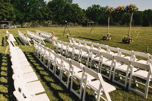 Sillas de jardín blanco de pie en filas ante un altar de boda — Foto de Stock
