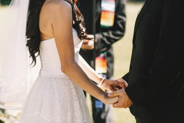 Fechar as mãos dos recém-casados segurando uns aos outros firmemente durante o — Fotografia de Stock