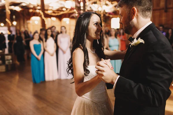 Gioiosa sposa ammira sposo mentre balla nella sala di legno piena — Foto Stock