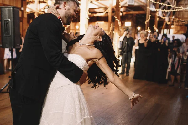 Bruidegom bochten brunette bruid tijdens het dansen in de houten hal — Stockfoto