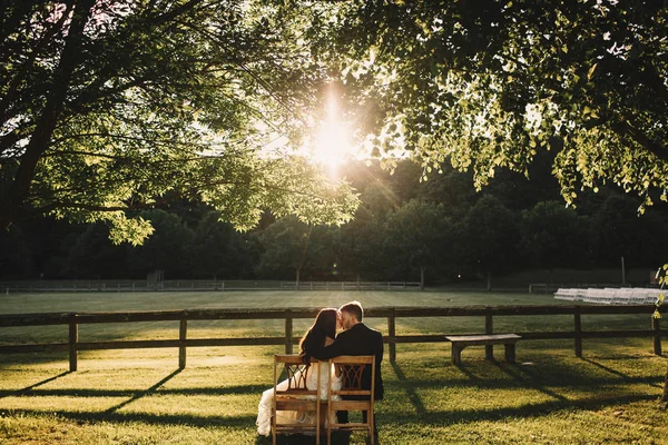 Groom hugs bride and kisses her while sitting in the rays of sun — Stock Photo, Image