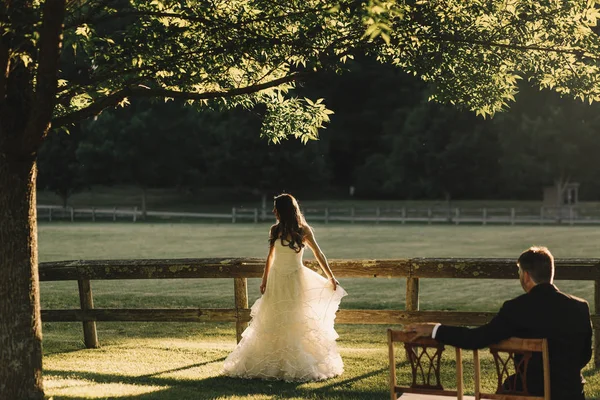 Bride whirls before a groom while he sits on the wooden chairs o — Stock Photo, Image