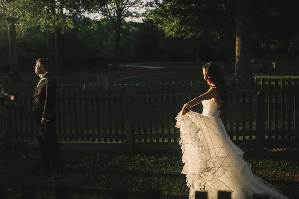 Kveldssolen skinner gjennom brudens kjole mens hun går på – stockfoto