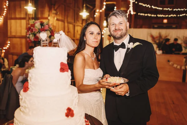 面白い新婚夫婦がウェディング ケーキを食べながらカメラにポーズします。 — ストック写真