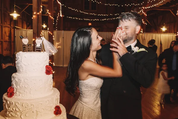 Sorridente sposa bruna mettere una torta nuziale sul viso dello sposo — Foto Stock
