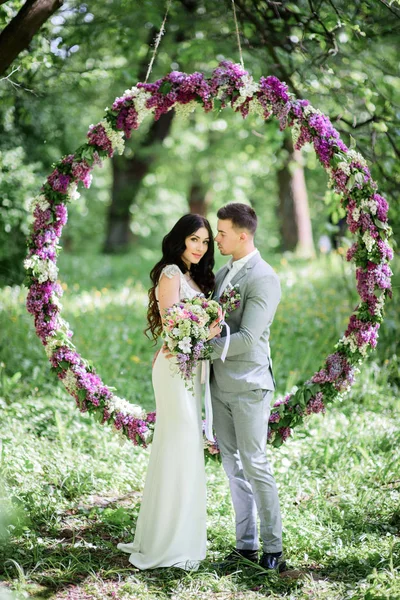 Casal elegante fica antes de grande círculo de lilás — Fotografia de Stock