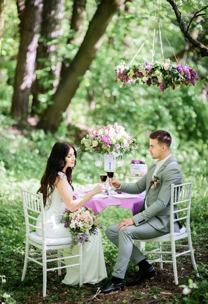 Lyckliga bröllopsparet sitter vid ett middagsbord med violett inredning i — Stockfoto