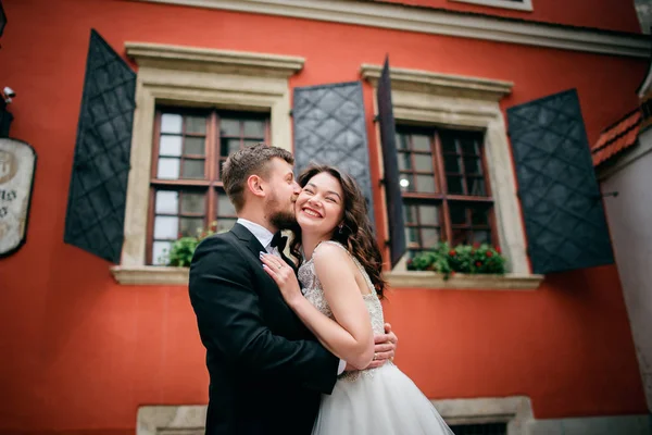 Hochzeitspaar umarmt sich vor orangefarbenem Haus — Stockfoto