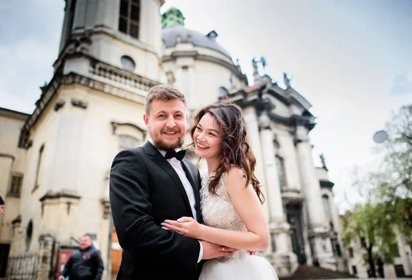 Hochzeitspaar posiert lächelnd vor alter Kirche — Stockfoto