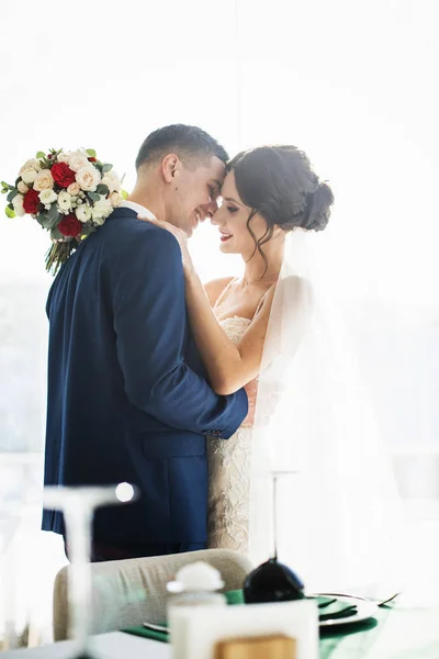 Sposa e sposo si abbracciano in piedi in sala luminosa — Foto Stock