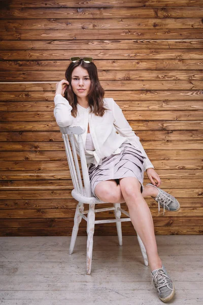 Una joven con el pelo largo, ropa blanca, en una silla y fondo de madera — Foto de Stock