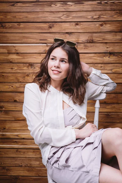 Una joven con el pelo largo, ropa blanca, en una silla y fondo de madera — Foto de Stock