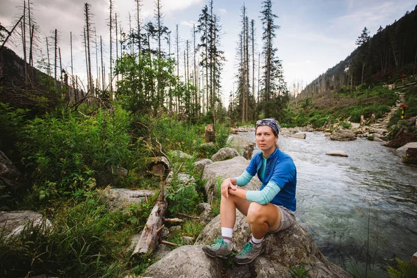 girl tourist Sedin on the stone near the mountain river in high Tatras in Slovakia. Dressed in a blue t-shirt, gray shorts, Hiking boots