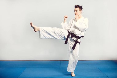 Kız karate gri arka planı stüdyosunda kimono uygun. Kadın çocuk gösterileri judo karate stans ile beyaz üniformalı siyah. Bireysel savaş sanatı spor. Tam vücut portre