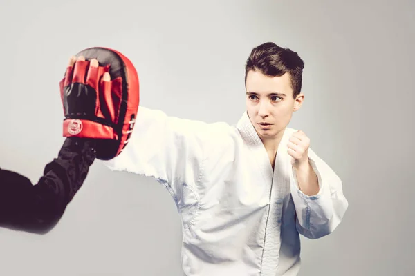 Chica en traje de karate kimono en estudio en fondo gris. La niña muestra judo o karate stans en uniforme blanco con cinturón negro. Deporte individual de arte marcial. retrato corporal — Foto de Stock