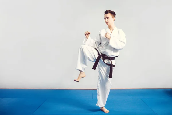 Chica en traje de karate kimono en estudio en fondo gris. La niña muestra judo o karate stans en uniforme blanco con cinturón negro. Deporte individual de arte marcial. retrato corporal — Foto de Stock