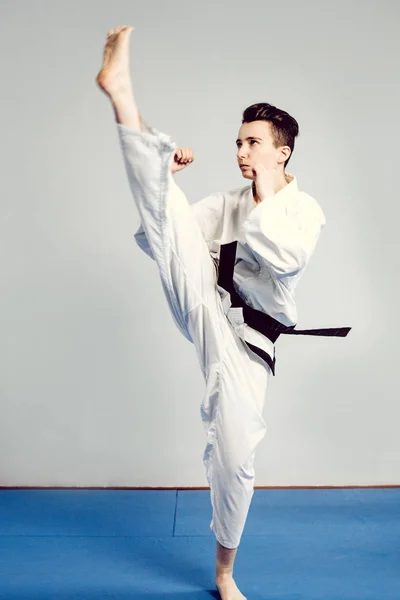 Chica en traje de karate kimono en estudio en fondo gris. La niña muestra judo o karate stans en uniforme blanco con cinturón negro. Deporte individual de arte marcial. retrato corporal — Foto de Stock